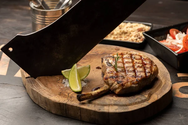Rib eye Bone steak and knife on wood wooden cutting board, tomatoes, lemon, rosemary