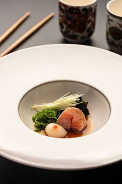 Beyaz seramik modern tabak çubukları ve fincanlar üzerinde sebzeli saşimi deniz tarağı.
