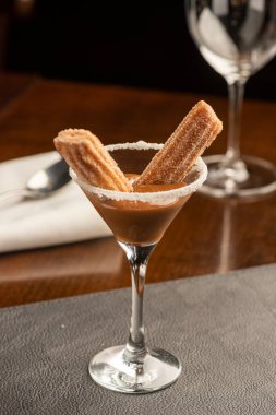 Mini churros with dulce de leche dessert on a glass on a blurred background with spoon and glass wine clipart