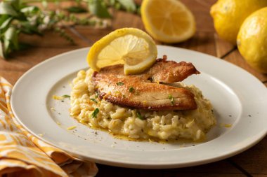 Beyaz tabakta risotto ile kabuklu beyaz tilapia balığı ve limon ve otlarla kaplı bulanık bir arka plan.