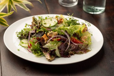 Beyaz tabakta sıralanmış sebzeli yeşil salata ve ahşap masa bardakları