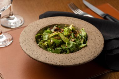 Karamelli fındıklı sezar salatası seramik kasede pastırma, peçete şarabı bardağı ve deri paspas.