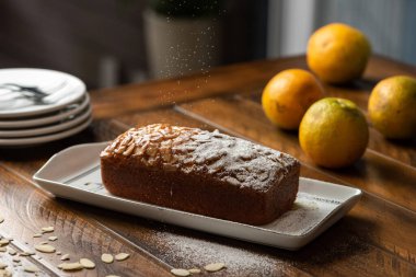 Portakal tabakları ve bulanık bir arkaplanı olan ahşap bir masada badem ve pudra şekerli turuncu pasta.