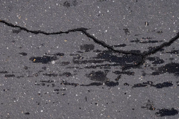 Eski çatlamış asfalt. Islak araba izleri var.