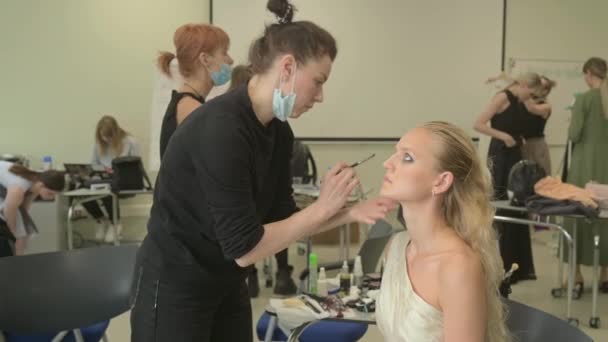 Os modelos fazem uma maquilagem e penteado antes de começar o desfile de moda SEMILETOVA. — Vídeo de Stock