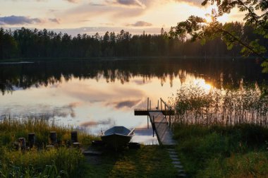 Küçük bir iskele ve bir tekne ile Finlandiyalı bir göl kıyısında yaz günbatımı.