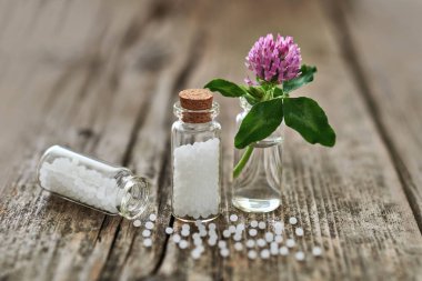 Küçük cam şişe, eski ahşap masa ve küçük bir çiçek üzerinde dağınık bazı granül Homeopatik granül.