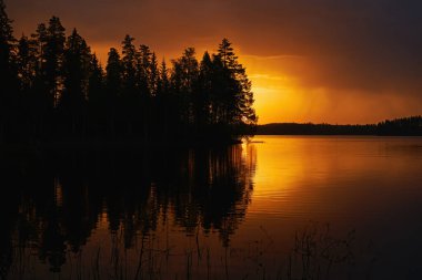 Göl, gökyüzü ve ağaçlarla gün batımında Finlandiya manzarası