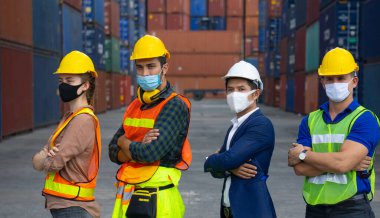 Coronavirus ya da COVID-19 maskesi takan sanayi işçileri ya da mühendisleri nakliye konteynerinin önünde duruyorlar..