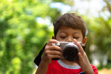 Asyalı çocuk halka açık parkta fotoğraf çekerken dijital kamera kullanıyor.