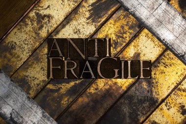 Klasik desenli gümüş grunge bakır ve altın arkaplan üzerine Anti Fragile metni oluşturan hakiki özgün yazı tiplerinin fotoğrafı