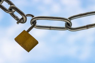 Krom asma kilit ve gerilmiş çelik zincirler kilitlenmeyi sembolize eden mavi bulutlu gökyüzüne yaklaşır.