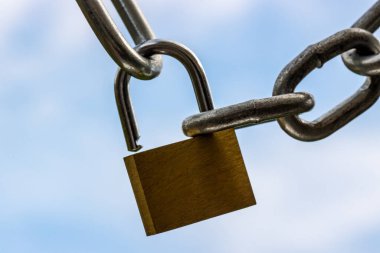 Krom asma kilit ve çelik zincirler kilitlenmeyi sembolize eden mavi bulutlu gökyüzüne yaklaşır.