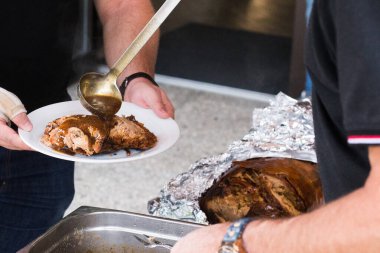 Izgara domuz yavrusu için sos servisi yapan bir adam. Üstünde deri olan bir yavru domuz..