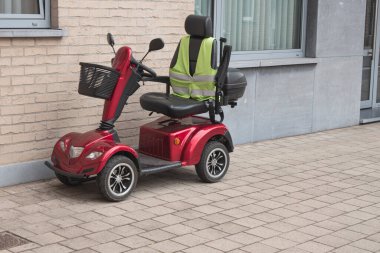 Evin ön cephesine park etmiş sarı florlu yelekli kırmızı dört tekerlekli bir scooter.