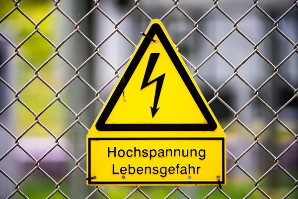 warning symbol for high voltage danger to life. yellow triangular warning sign in german on fence of power plant. yellow