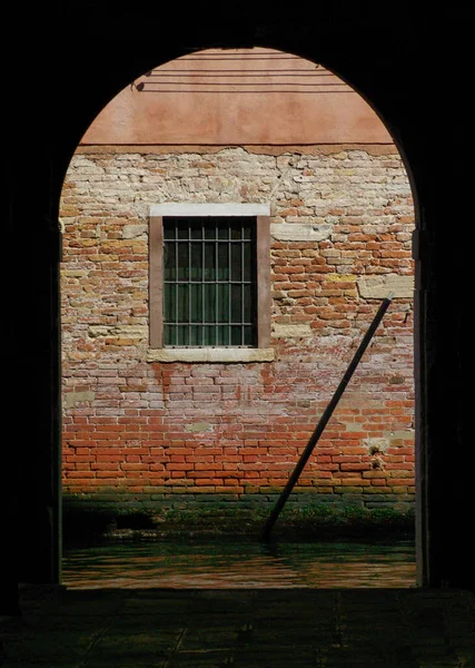 Eski kırmızı duvara ve parmaklıklı pencereye açılan kemerli kapı. — Stok fotoğraf