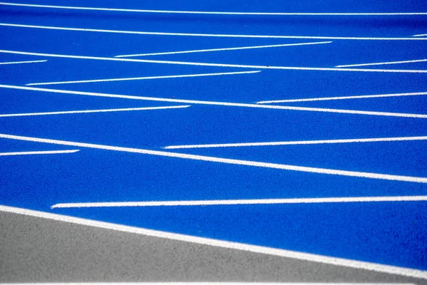 Linhas brancas na superfície texturizada da pista de corrida azul. — Fotografia de Stock