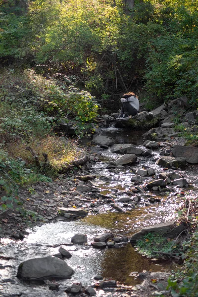 Jovem triste senta-se sozinho por um riacho de floresta cobrindo seu rosto. — Fotografia de Stock