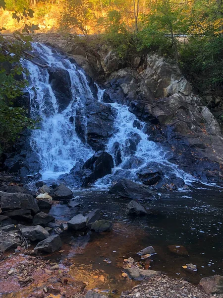 Die Sonne geht hinter einem Wasserfall unter, Herbstlaub und schwarze Felsen. — Stockfoto