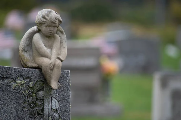 Sad stone angel sits atop a cemetery tombstone — Stock Photo, Image