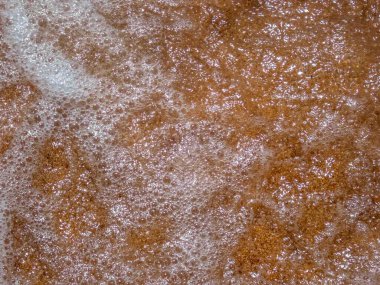 Yüksek açılı dalgaların kumlu, sıcak sahil baloncukları ve turuncu kumun üzerindeki deniz köpüğü üzerindeki güneş ışığını yansıtan dalgalar..