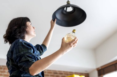Woman changing lightbulb at home  clipart