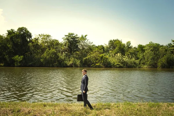 自然の中で実業家迷う男湖に立って押しブリーフケース — ストック写真