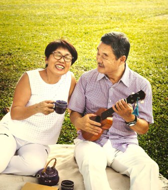 Asyalı Olgun çift harcamak zaman birlikte parkta çay bardağı, ukulele oynayan adam tutan kadın