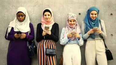 İslam kadın akıllı kullanarak grubu ayakta gri duvarının yakınında telefonları