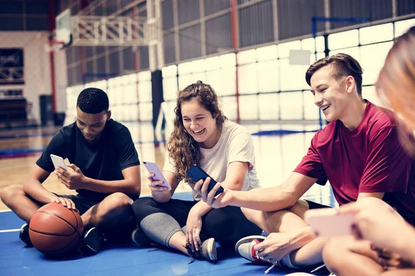 一群年轻的青少年朋友在一个篮球场放松和使用智能手机 — 图库照片