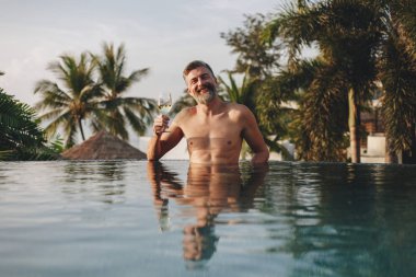 Bir bardak şarap havuza sahip yakışıklı adam