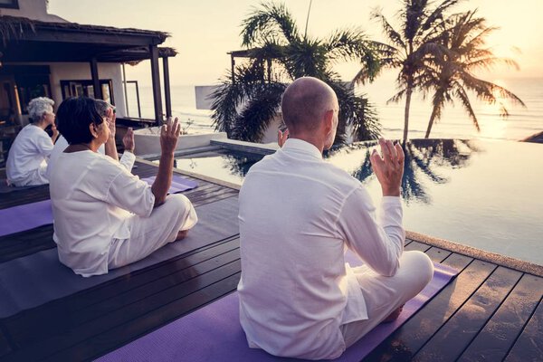 Group of seniors practicing yoga by the pool