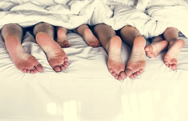 Whole family sharing a bed, view of feet under the blanket