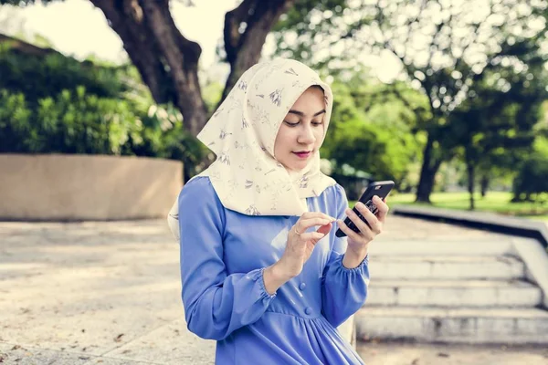 Parkta bir akıllı telefon kullanan Müslüman kız