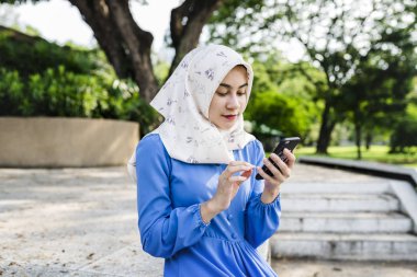 Parkta bir akıllı telefon kullanan Müslüman kız