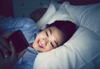 Asyalı kadın yatakta telefonunu kullanarak
