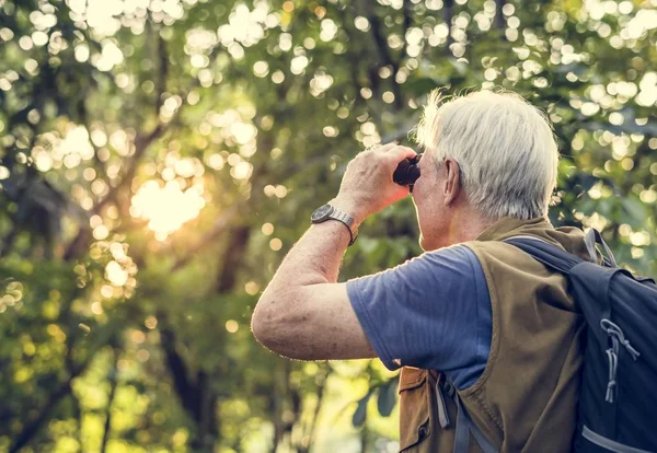 Elderly man watching with binoculars in forest