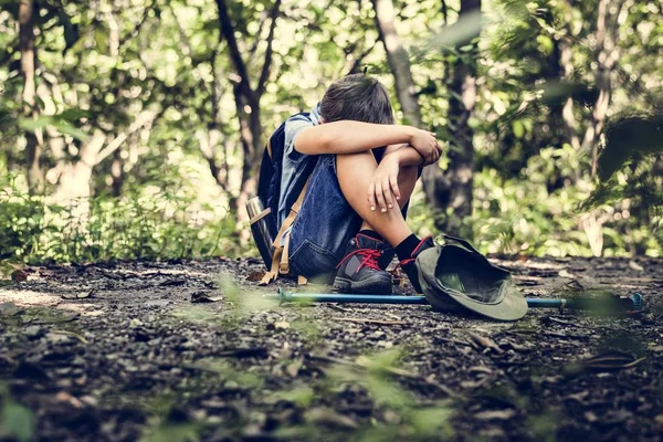 Little boy lost in forest and sad sitting on ground hugging knees