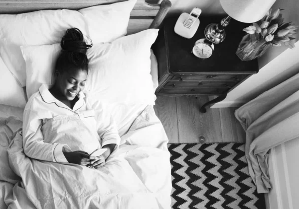 Χαμογελώντας Αφρικανική Αμερικανική Γυναίκα Στο Κρεβάτι Χρησιμοποιώντας Ένα Κινητό Τηλέφωνο — Φωτογραφία Αρχείου