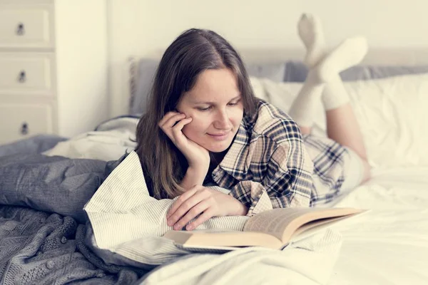 早晨在床上微笑的年轻妇女读书书 — 图库照片