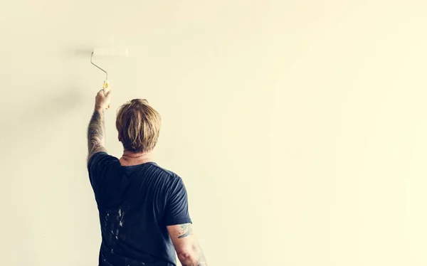 Чоловік з татуюванням, що тримає ролик, фарбує стіну — стокове фото