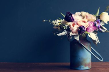 Tahta masadaki metal vazoda çeşitli taze çiçekler düzenleniyor.