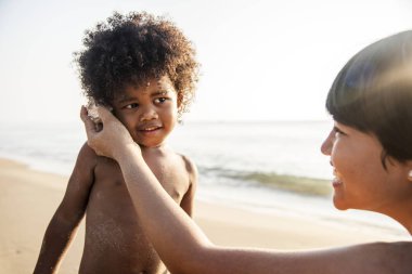 sevimli çocuk annesiyle kumsalda kabuk içinde okyanus dalgaları dinlerken