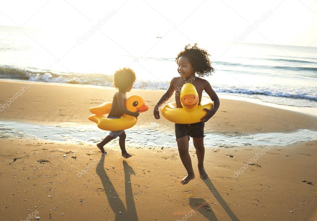 Little brothers having fun with inflatable duck tubes on beach in evening