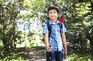 Küçük çocuk sırt çantası ve kırmızı bayrak, bir orman yoluyla hiking uzağa arıyorsunuz 