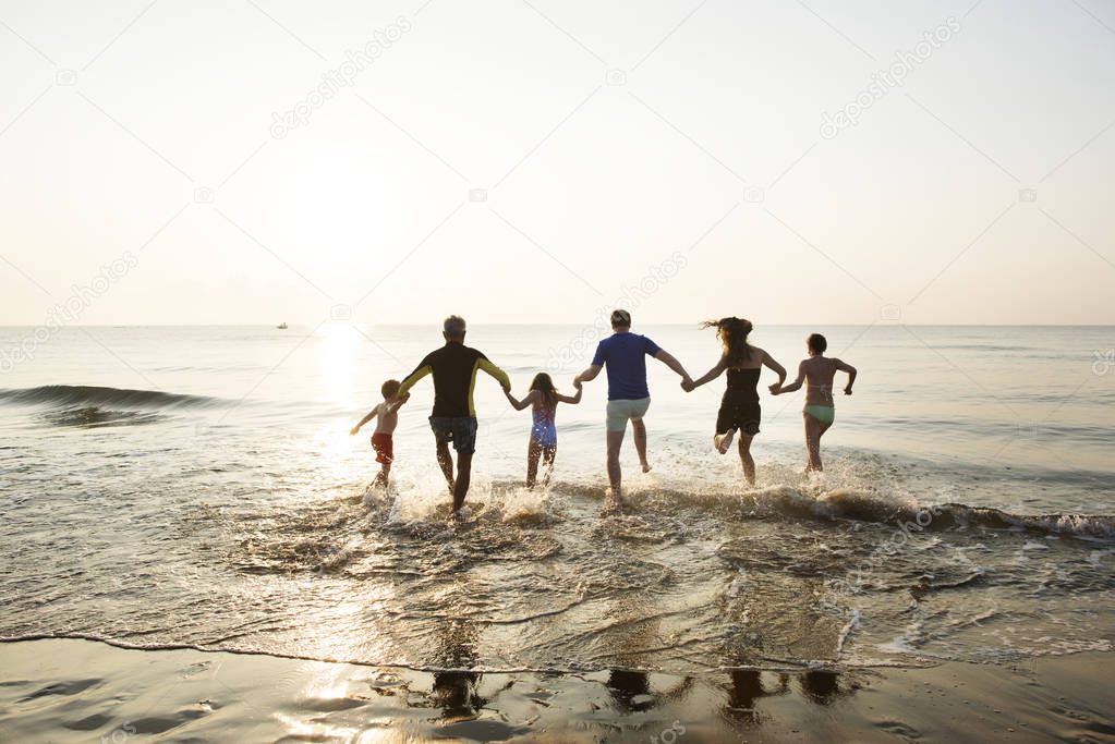 rear view of big family playing running into sea in front of sunset sky