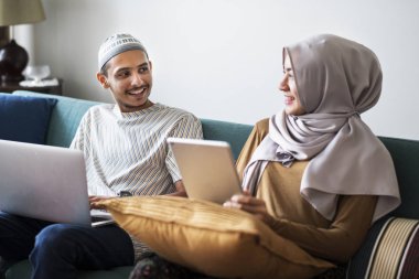 Muslim family using digital devices at home clipart