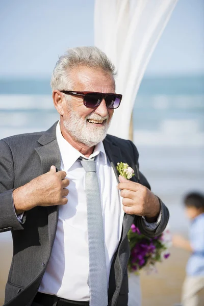 happy senior groom in suit and sunglasses at beach wedding