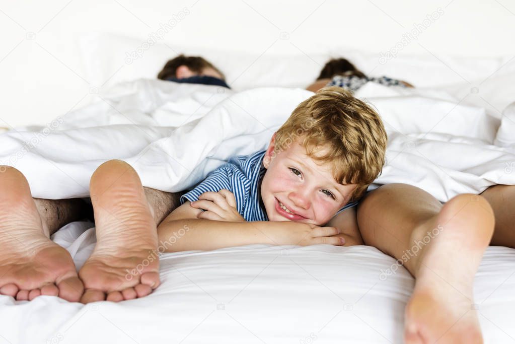 adorable little kid lying in bed with parents and looking at camera